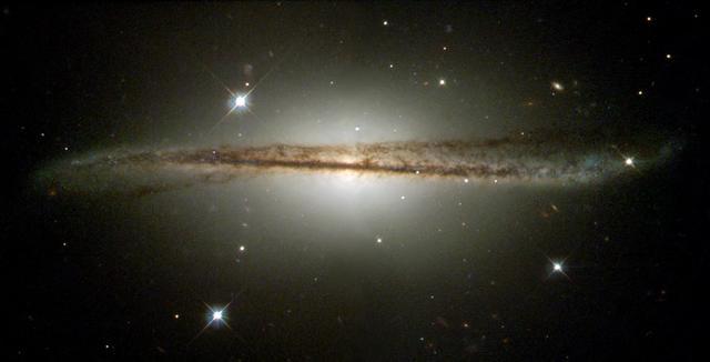 Edge on image of galaxy ESO 510-G13. A thin band of brown clouds that is brighter in the middle against a black background